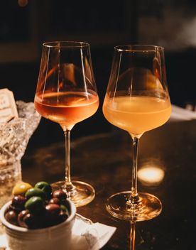 Two glasses of natural wine sitting on a darkly lit bar next to a small cup of green olives.