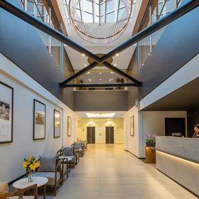 The vast lobby of Oaks Wellington, with very high ceilings, the reception desk to the right and the seating area to the left.