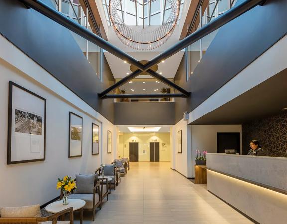 The vast lobby of Oaks Wellington, with very high ceilings, the reception desk to the right and the seating area to the left.