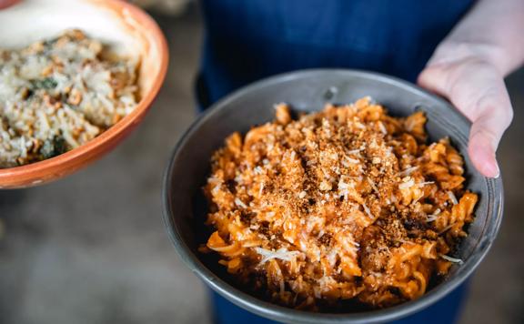 Close-up of waiters hands holding two pasta bowls at 1154 Pastaria on Cuba Street. Focused in the foreground is a bowl of spiralled pasta.