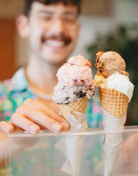 Two double scooped gelato in waffle ice cream cones set in a clear plastic stand at Raglan Roast Coffee at Chaffers Dock in Te Aro in Wellington. The smiling worker is our of focus but visible behind the ice cream.