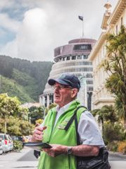 A person in a green vest speaks to someone off camera. The Beehive is in the background.
