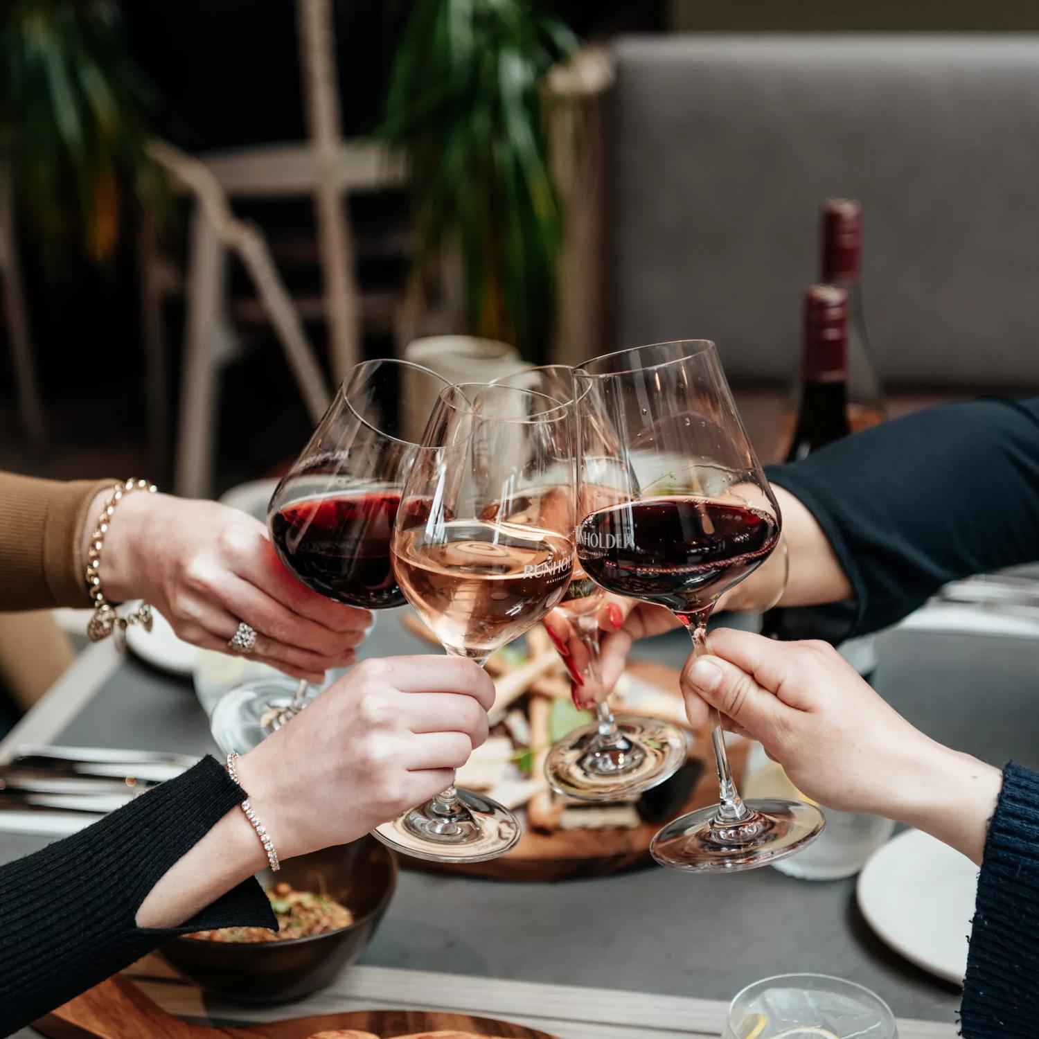 Four people hold out their wine glasses for a toast at The Runholder, a restaurant, tasting room, cellar door, and distillery in Martinborough.