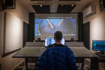 A crew member at Pow Studios working on sound for a movie in front of a large desk with many dials.