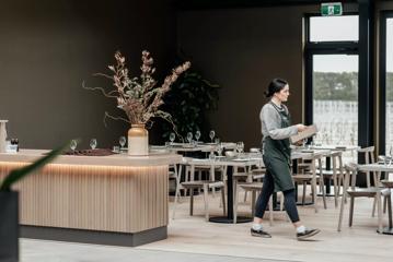 A server wearing a striped shirt and green apron walks across the empty, set dining room at The Runholder, an upscale restaurant in Martinborough.