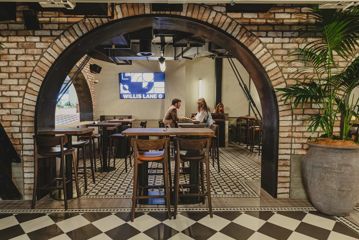 Looking into a brick archway at 4 people sitting on a high table with food.