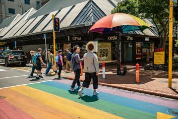 2 people walking across the rainbow crossing on Cuba street, next to the rainbow umbrella.