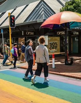 2 people walking across the rainbow crossing on Cuba street, next to the rainbow umbrella.