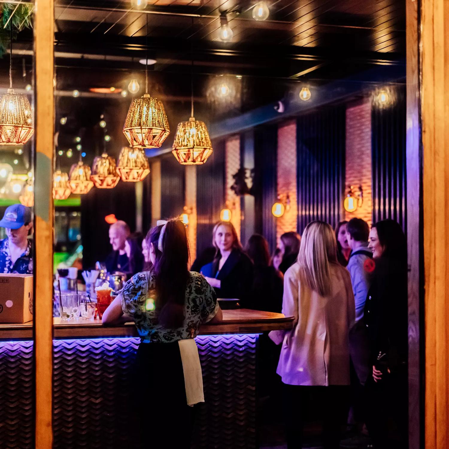 Looking into the open glass doors at Lulu Bar, workers and patrons are standing by the counter in the dark, amber-lit space.