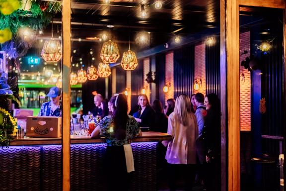 Looking into the open glass doors at Lulu Bar, workers and patrons are standing by the counter in the dark, amber-lit space.