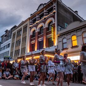 A group of dancers in silver costumes are preforming on the street at CubaDupa.