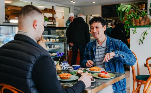 Two customers dining at a table inside Uncle Leo’s Bakery, with food, drinks, and the bakery counter visible in the background.