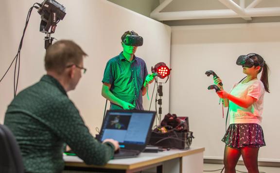 Two people are using virtual reality equipment while another is seated at a desk using a laptop at a production space at Victoria University in Wellington.