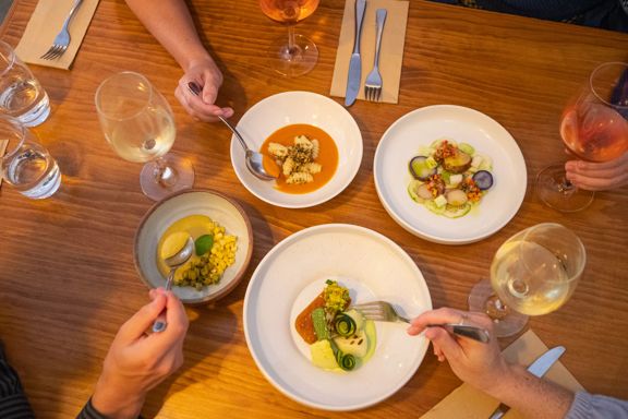 Four fine dining dishes on a table with people's hands reaching in with utensils.