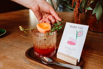 A Guava Fizz mocktail in a fluted tumbler glass on a small wooden tray.