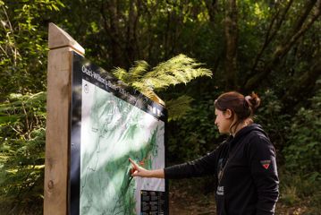 A section of trail Te Ara o Tama in Ōtari-Wiltons Bush. A person is pointing at the path on a green and white sign.