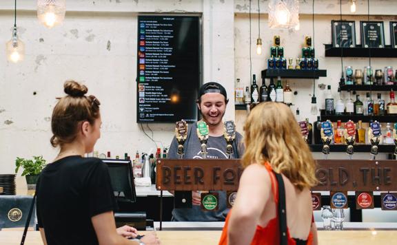 Inside Fortune Favours, a bar located in Te Aro, Wellington. Two people are standing at the bar, waiting while a smiling bartender pours them a pint.  