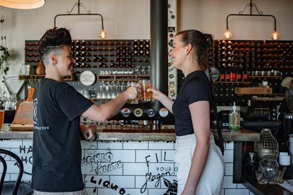 Two people clink glasses at North End Brewery with a wall of bottles filling the back wall behind them.