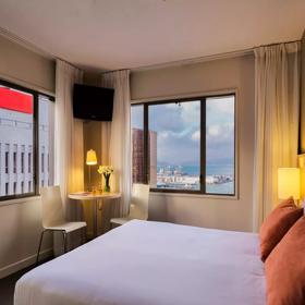 A guest room in the Travelodge Hotel has a bed with crisp white sheets, and the window has views of Wellington harbour.