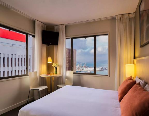 A guest room in the Travelodge Hotel has a bed with crisp white sheets, and the window has views of Wellington harbour.