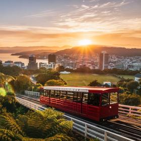 Wide of the cable car driving up the tracks with the sun setting over Wellington city and harbour in the background.