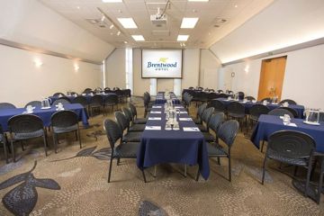 Rectangle shaped room with 50 chairs around 8 tables facing towards a projector at the front of the room.