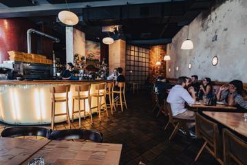 Inside Scopa, an Italian restaurant in Te Aro, Wellington. People are eating at the tables and an open pizza kitchen in the middle of the space.