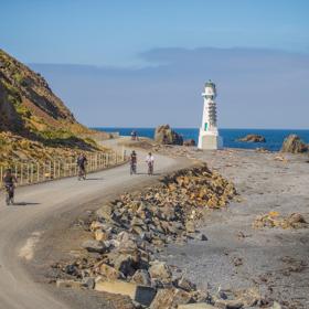 Cyclists are riding along a coastal road at the Pencarrow Coast in Eastbourne, New Zealand.