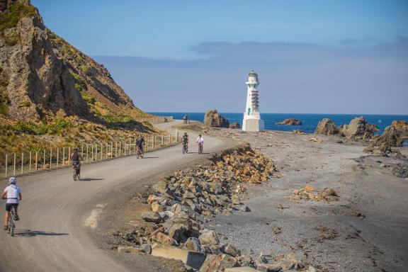 Cyclists are riding along a coastal road at the Pencarrow Coast in Eastbourne, New Zealand.