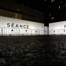 Two white shipping containers, one has Séance written on it and the other has Flight.