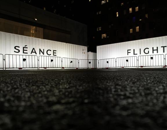 Two white shipping containers, one has Séance written on it and the other has Flight.