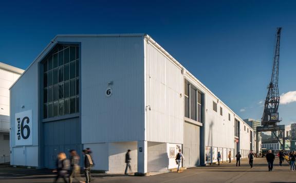 The exterior of Shed 6 on Queens Wharf, with people walking along the wharf in front.