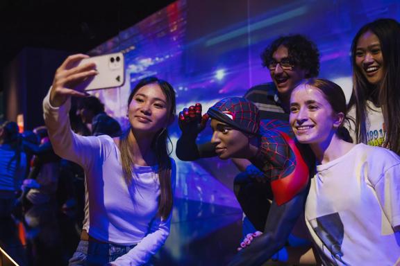 Four teenagers are standing around a statue of Spiderman, taking a selfie at Marvel Earth's Mightiest Exhibition Tākina Wellington Convention & Exhibition Centre.