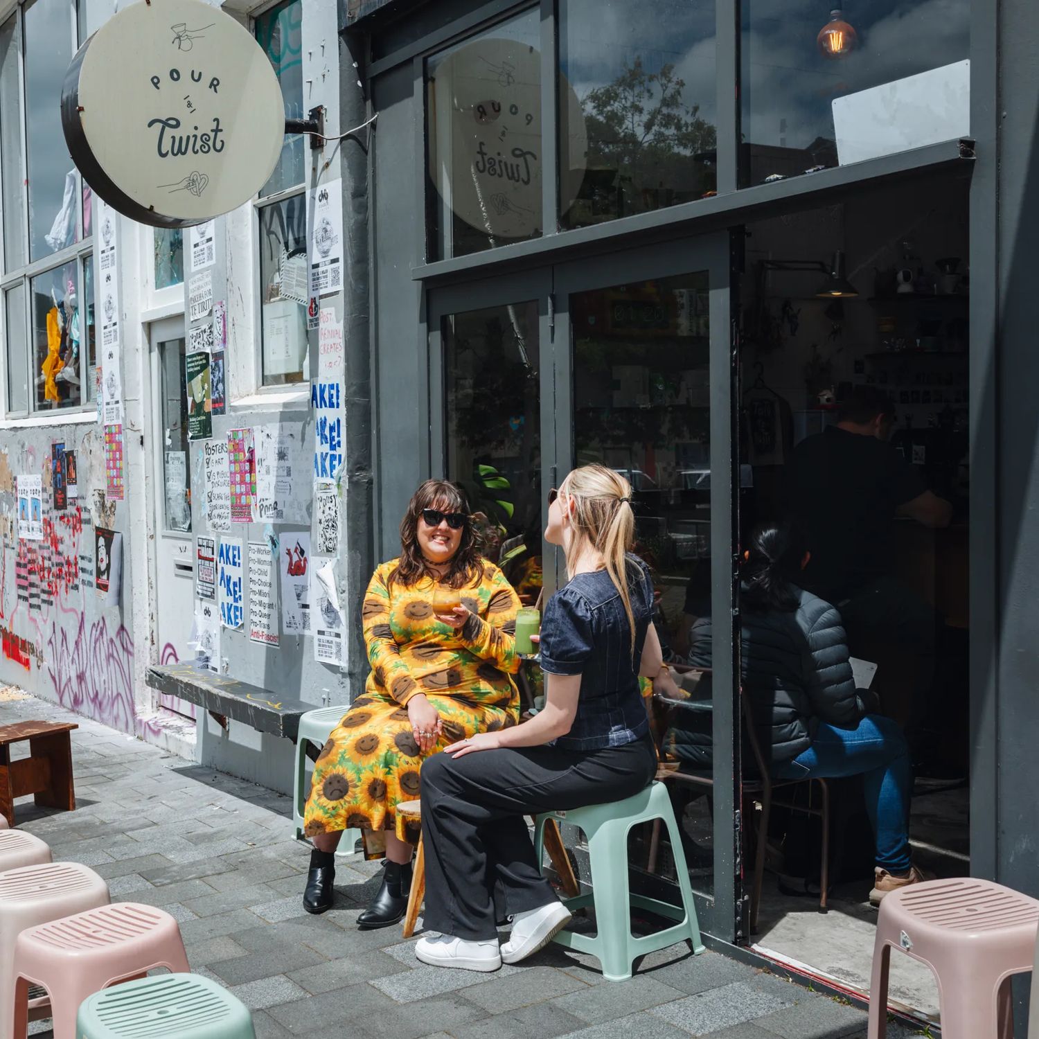 Two friends enjoy iced coffees on the exterior seating at Pour & Twist on a sunny day.