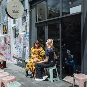 Two friends enjoy iced coffees on the exterior seating at Pour & Twist on a sunny day.