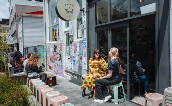 Two friends enjoy iced coffees on the exterior seating at Pour & Twist on a sunny day.