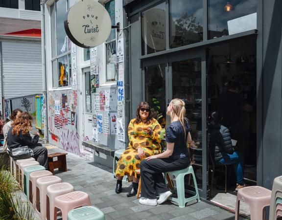 Two friends enjoy iced coffees on the exterior seating at Pour & Twist on a sunny day.