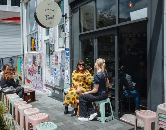Two friends enjoy iced coffees on the exterior seating at Pour & Twist on a sunny day.