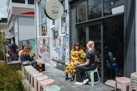Two friends enjoy iced coffees on the exterior seating at Pour & Twist on a sunny day.