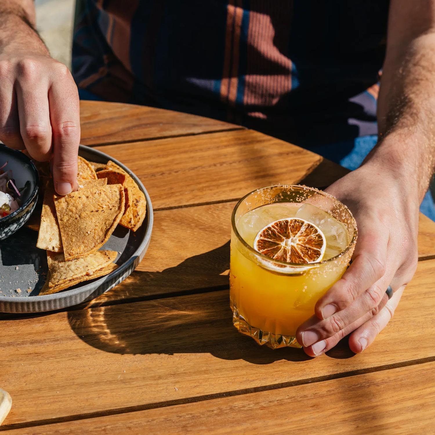 A plate of ceviche and chips, and a cocktail on a table.