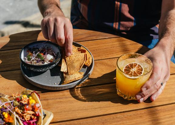 A plate of ceviche and chips, and a cocktail on a table.