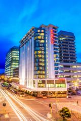 The Rydges Wellington building at night. It's a large white and glass building on a busy city corner.