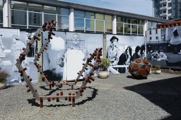 Image of the sculpture yard behind Suite Gallery. The walls are  covered in huge black and white photographic images. The ground is covered in gravel and has two large corten steel sculptures.