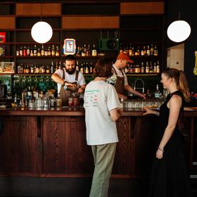 Inside Regent, a cocktail pub in Te Aro Wellington, where four patrons stand by the bar to order drinks while two bartenders are working.