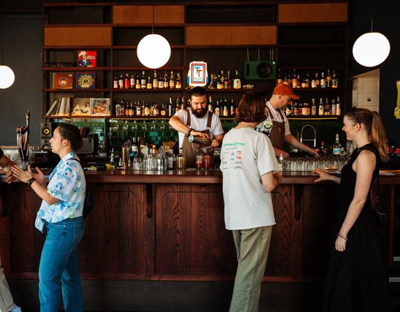 Inside Regent, a cocktail pub in Te Aro Wellington, where four patrons stand by the bar to order drinks while two bartenders are working.