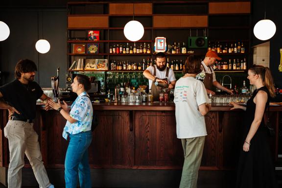 Inside Regent, a cocktail pub in Te Aro Wellington, where four patrons stand by the bar to order drinks while two bartenders are working.