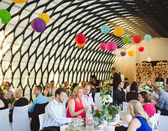 People are seated at two long tables with white tablecloths in the Kamala function room at Wellington Zoo. Colourful lanterns hang from the intricate metal ceiling.