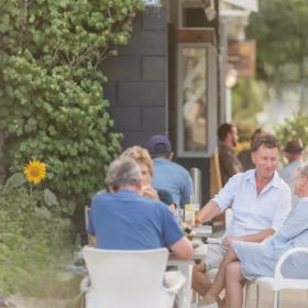 Four adults sit together at a table on the patio at Long Beach Tavern,  located in Waikanae Beach, New Zealand.