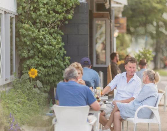 Four adults sit together at a table on the patio at Long Beach Tavern,  located in Waikanae Beach, New Zealand.