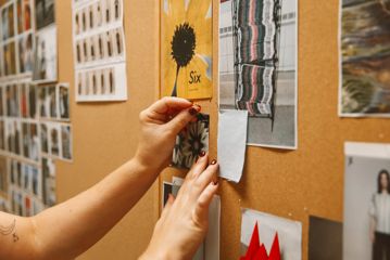 A person pins an image to a corkboard.
